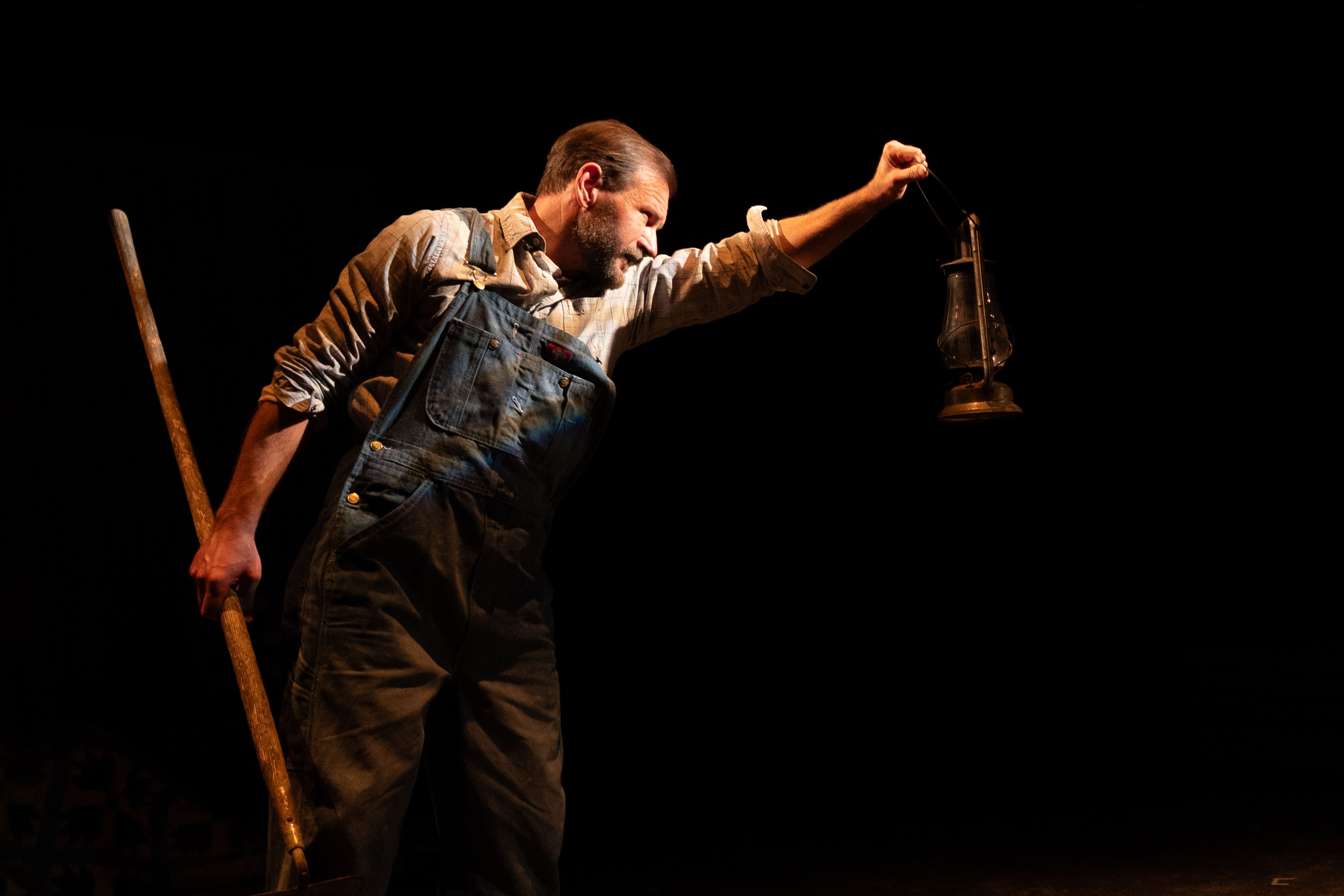 Man in overalls holding a lantern in the dark.