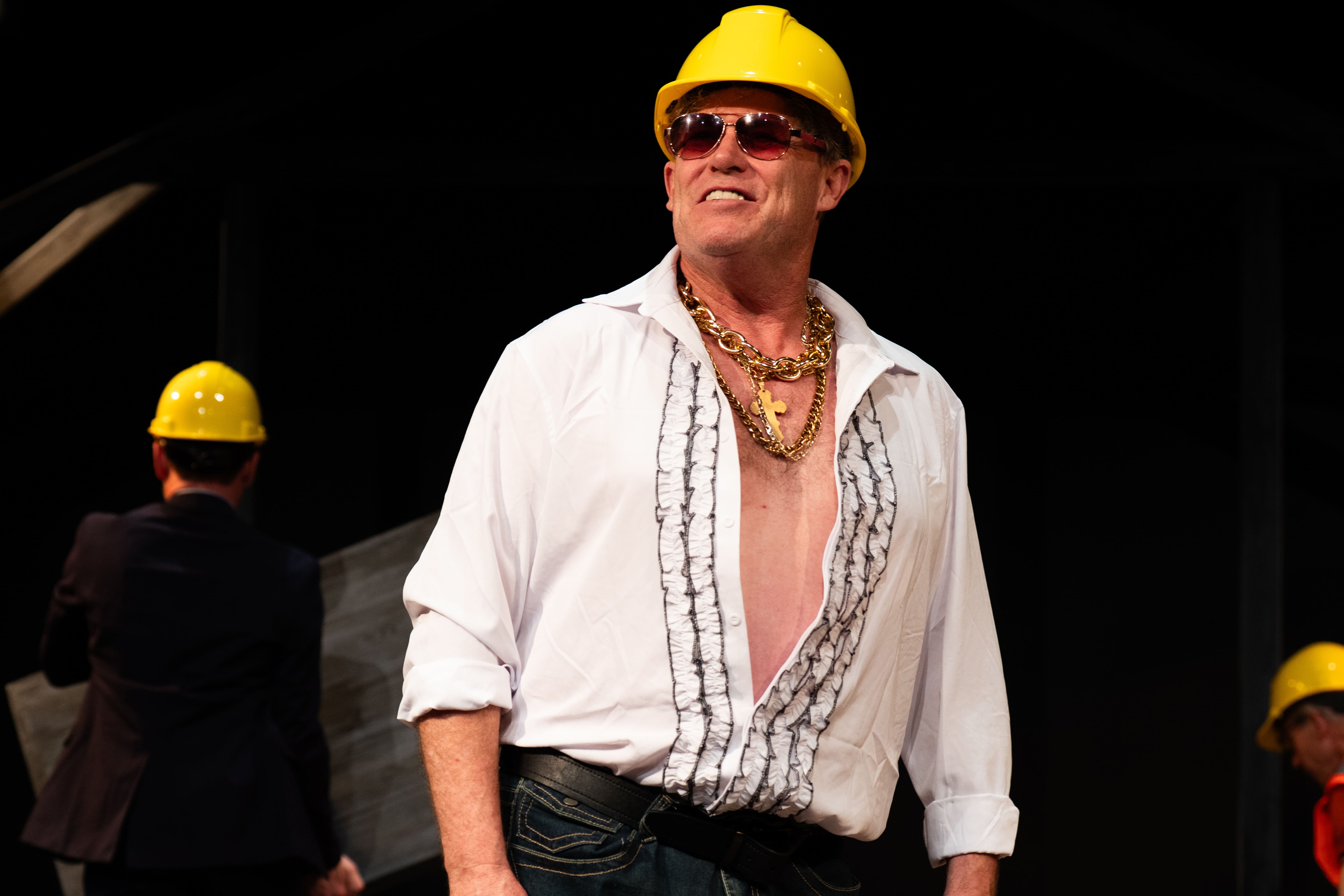 Man in a white open shirt and yellow helmet posing confidently.