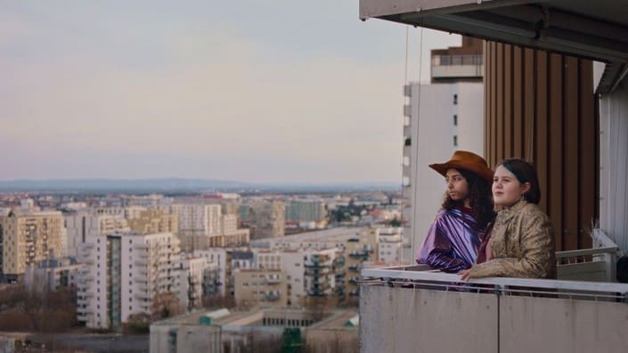 Person in a hat enjoying city view from a balcony.