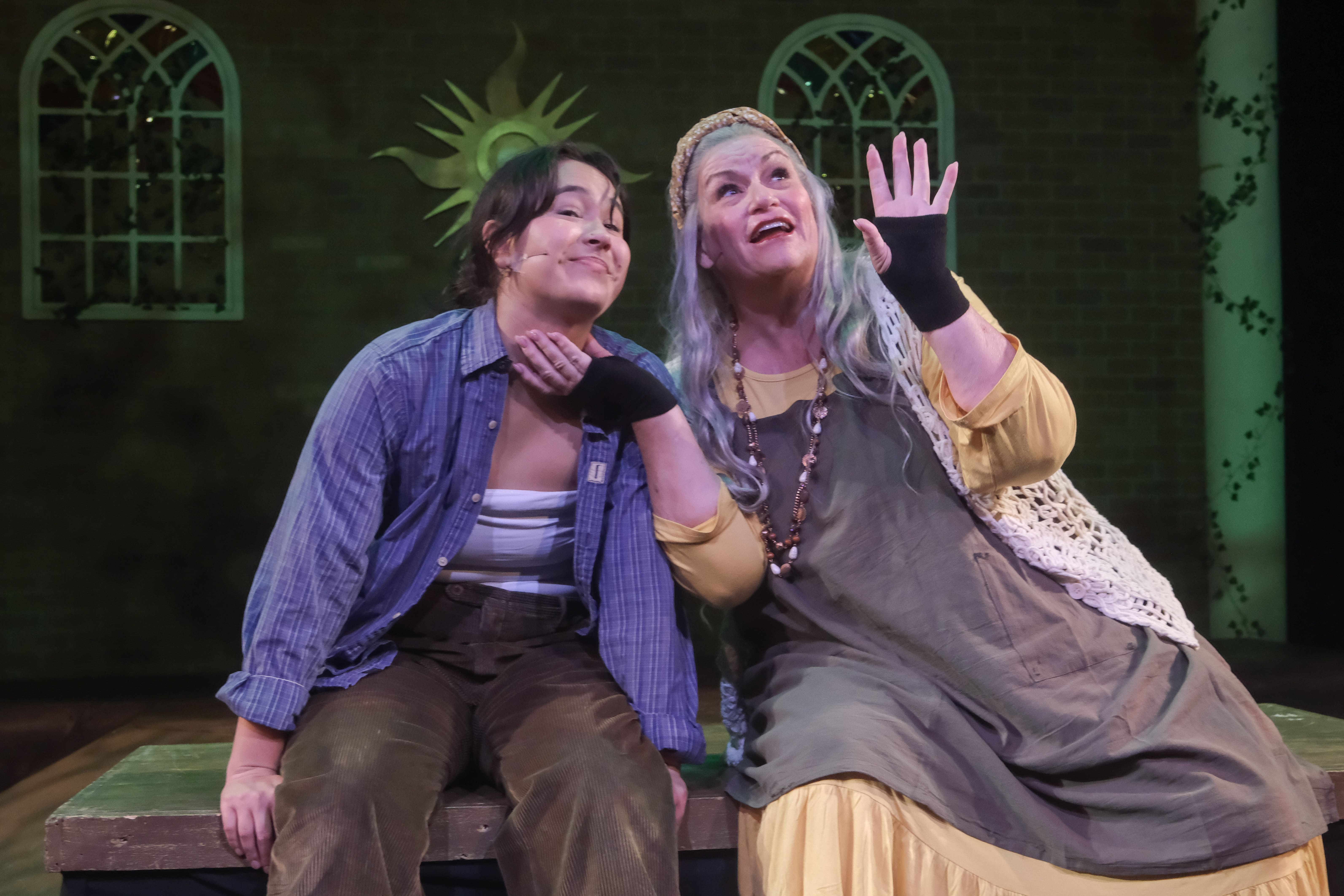 Two women in theatrical costumes share a joyful moment on stage.