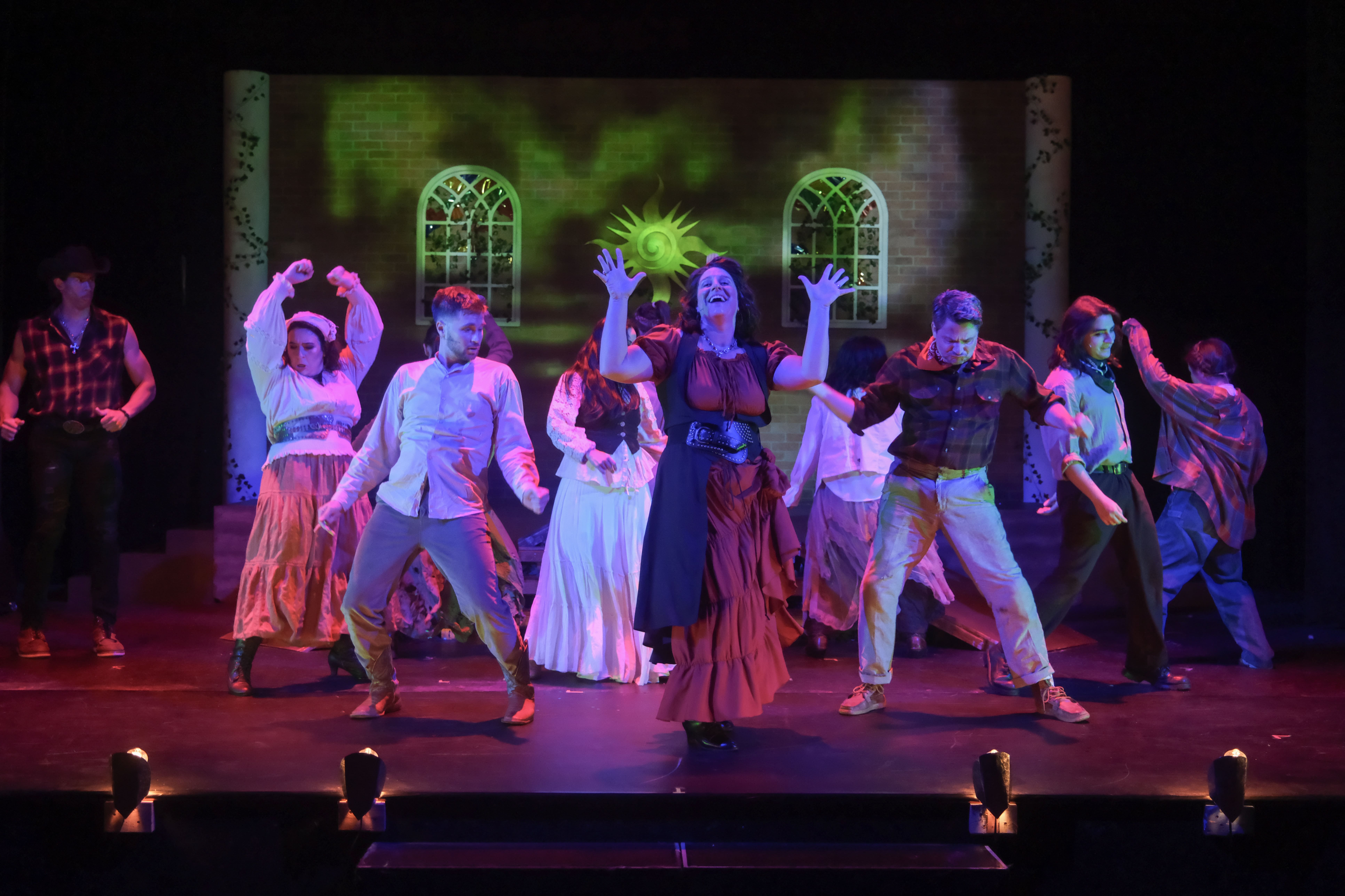 A group of performers in colorful costumes dance on stage with a vibrant backdrop.