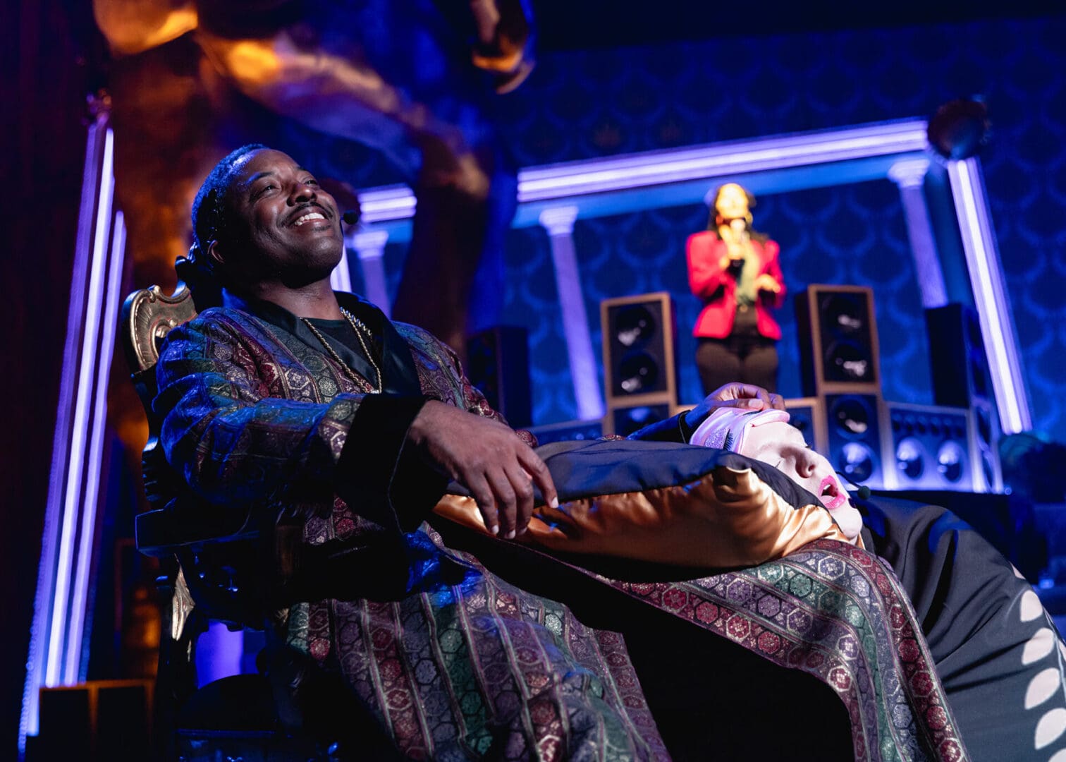 Man in colorful robe reclining comfortably with a smile in a dimly lit room.