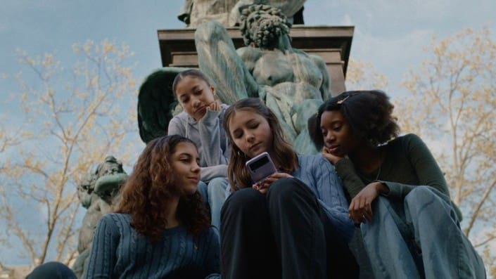 Four girls looking at a phone together near a statue.