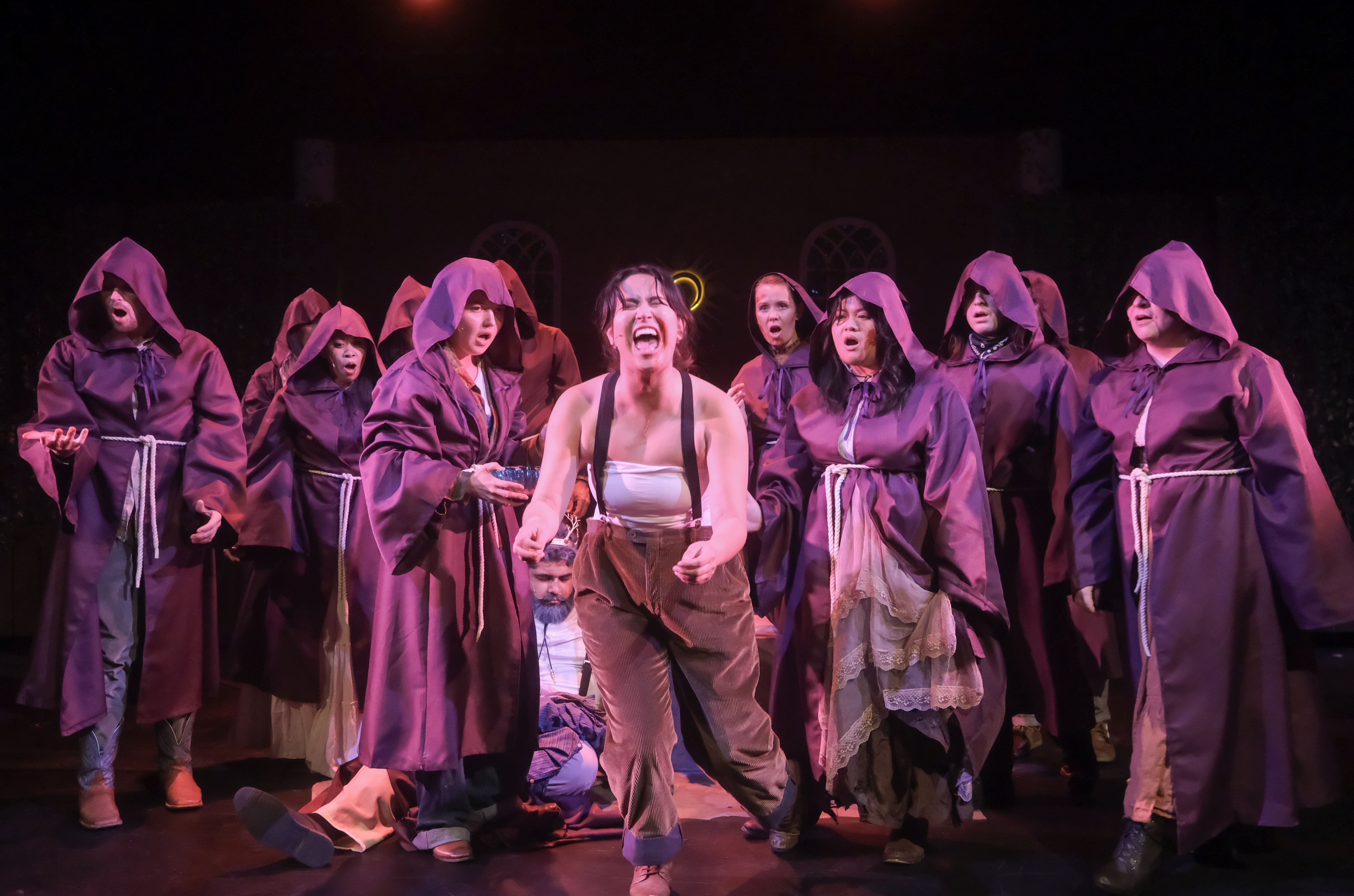 A theatrical group performs a dramatic scene with one central character in front.