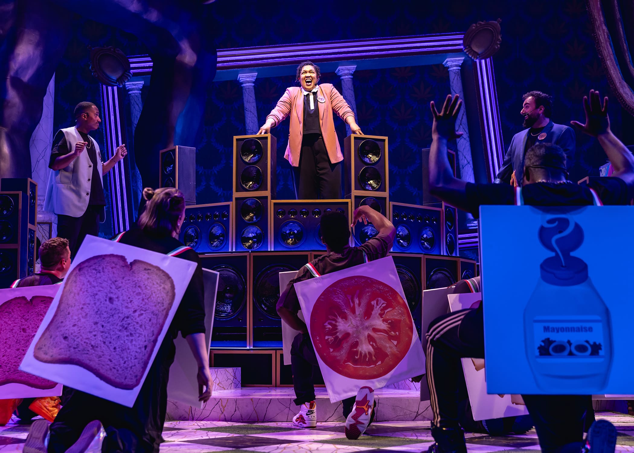 Actors on stage performing a vibrant, playful scene with oversized food props.