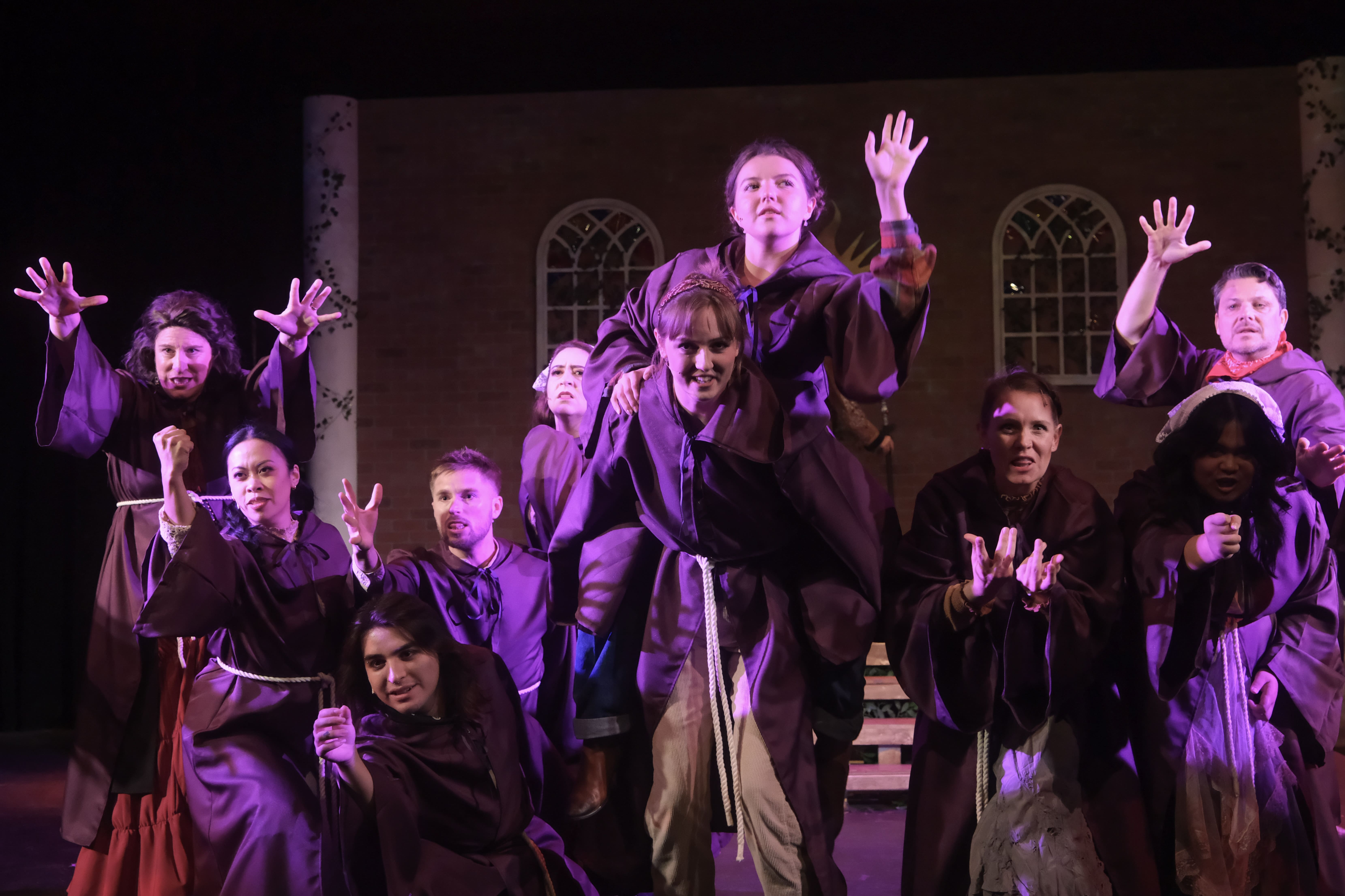 A group of performers in dark costumes pose dramatically on stage.