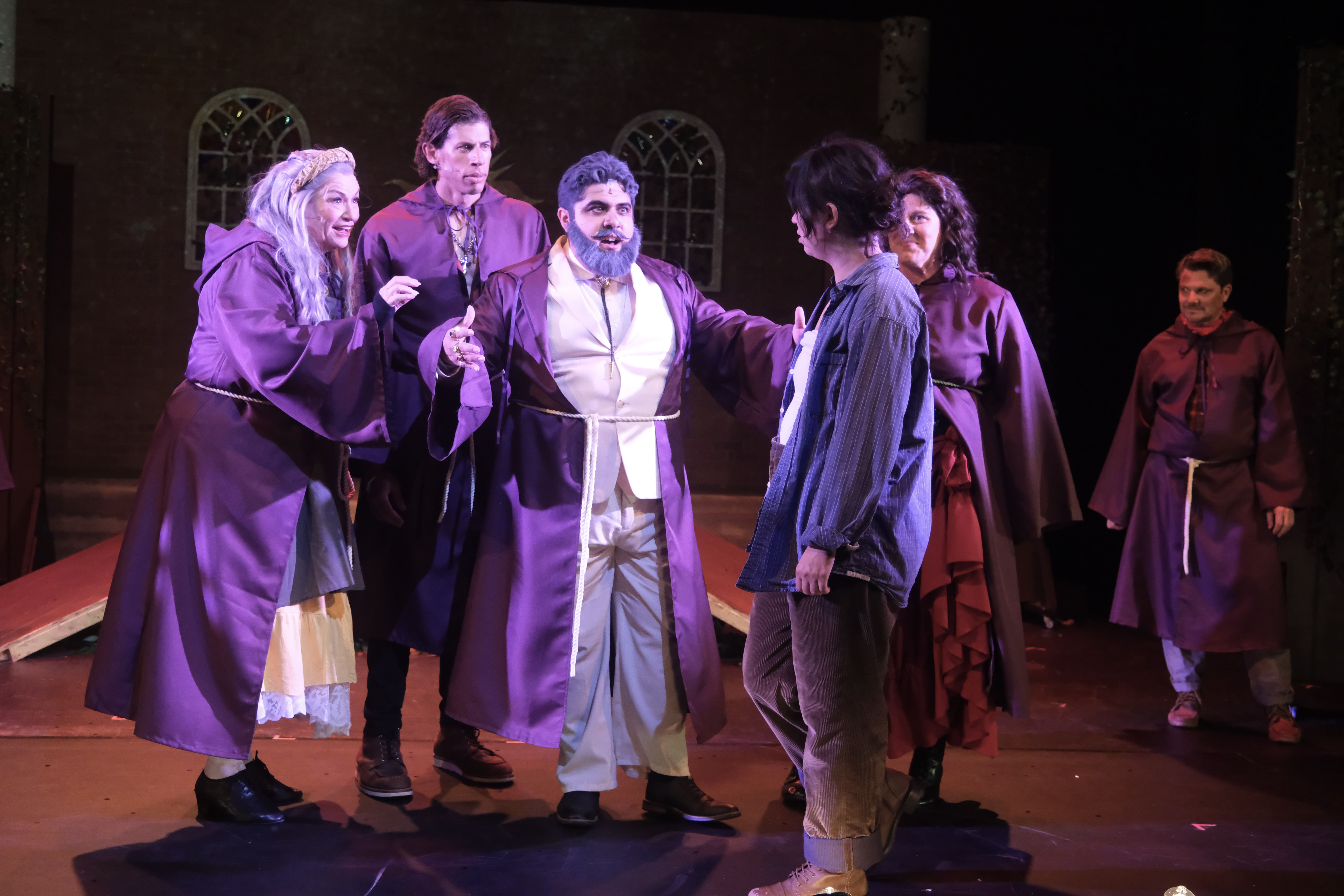 Actors performing a dramatic scene on stage in period costumes.