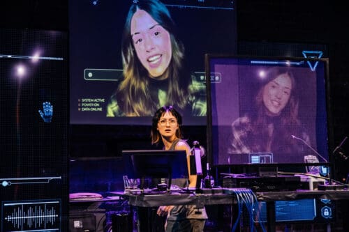 A woman presenting with her image projected behind her on screens.