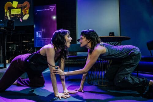 Two women engaged in an intense, close conversation on stage.