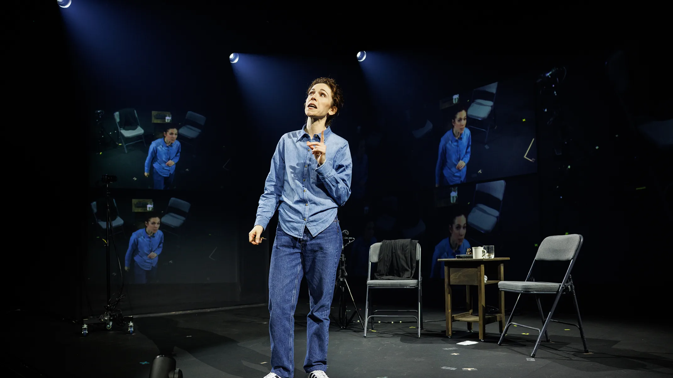 A person performing on stage with multiple screens showing their image.