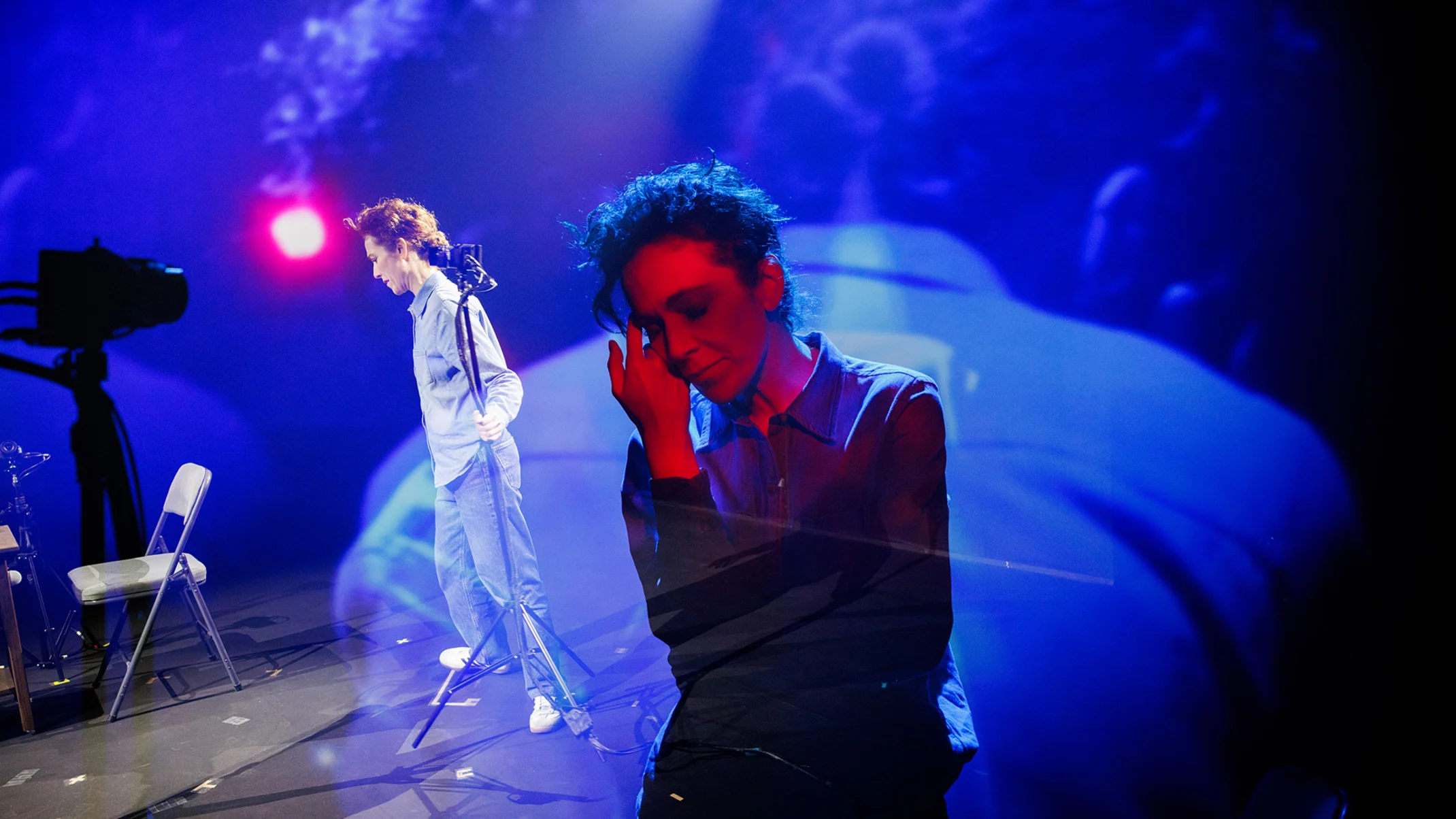 Two performers on stage with dramatic blue and purple lighting.
