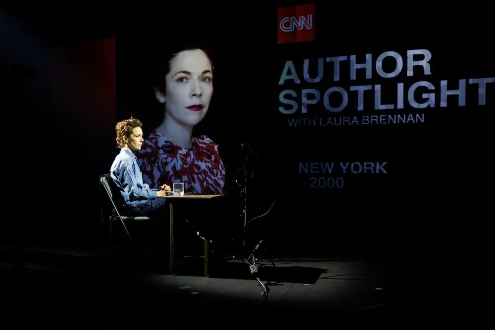 A presenter speaks at a CNN event with a large portrait and logo in the background.