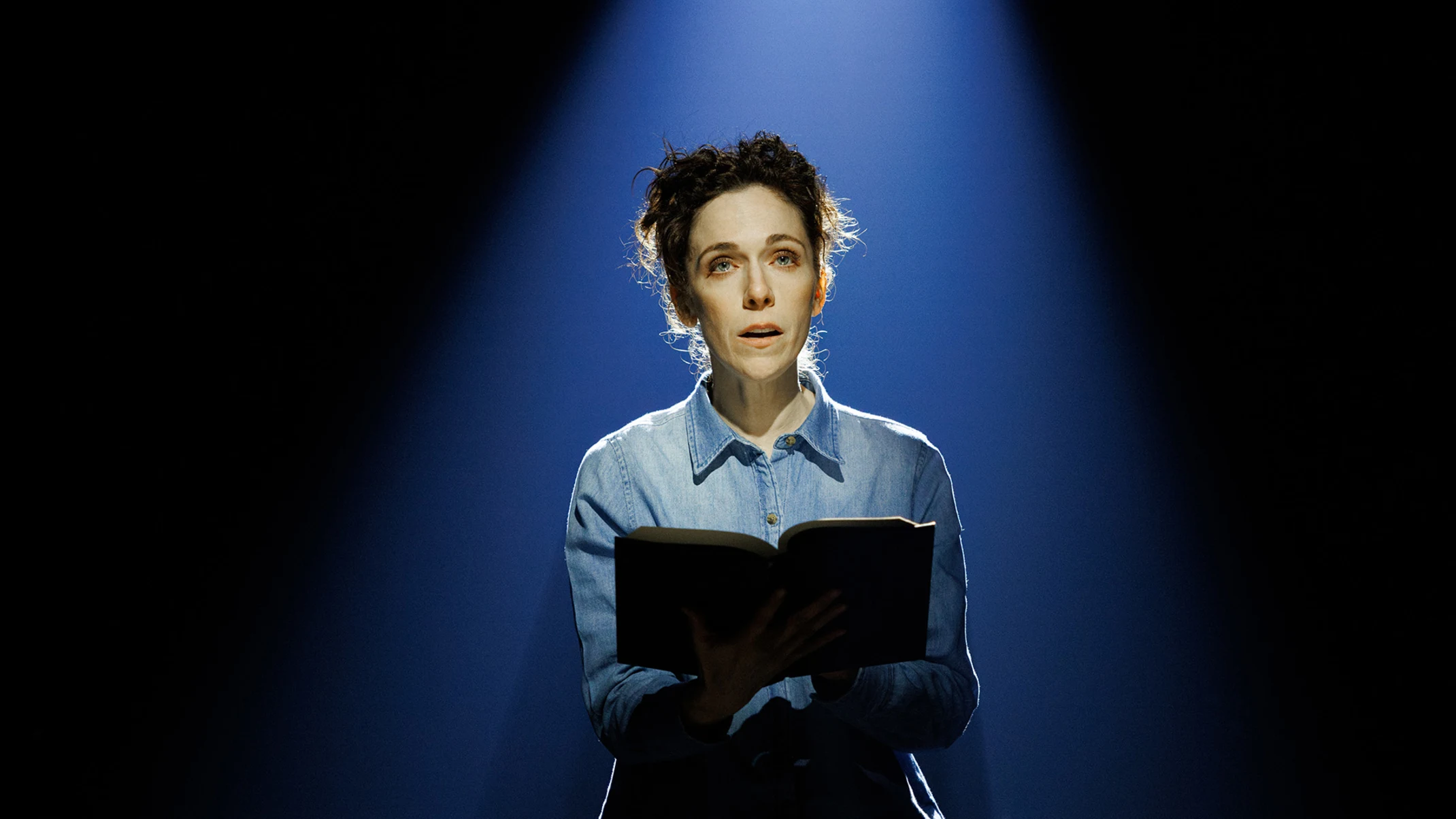 A woman reading a book under a spotlight.