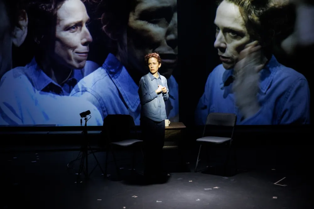 Person standing on stage with large projected faces behind them.