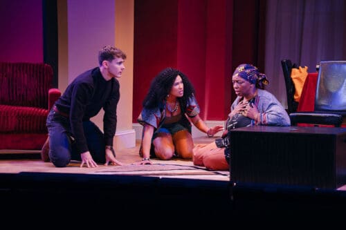 Three actors engaged in an intense theatrical scene on stage.