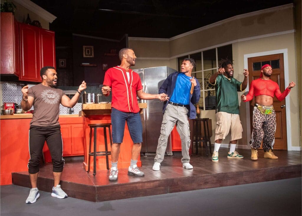 Five actors performing energetically on stage in casual attire.