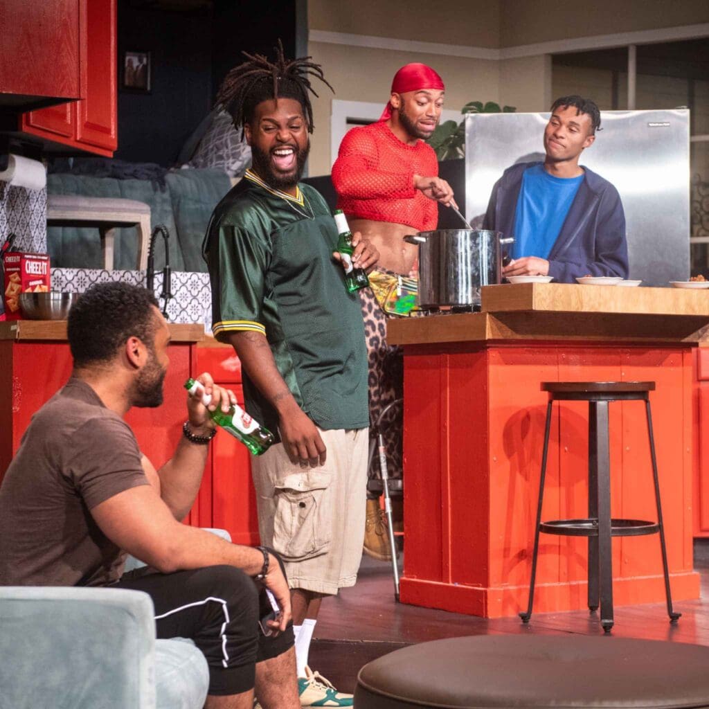 Four men casually chatting and laughing in a kitchen setting.
