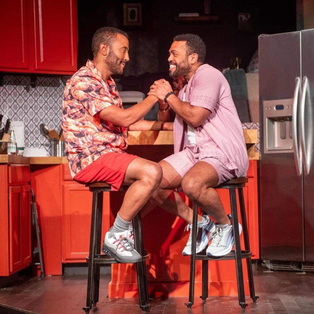 Two men smiling and shaking hands in a kitchen setting.