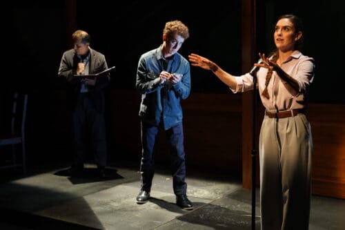 Actors perform an intense scene on stage with dramatic lighting.