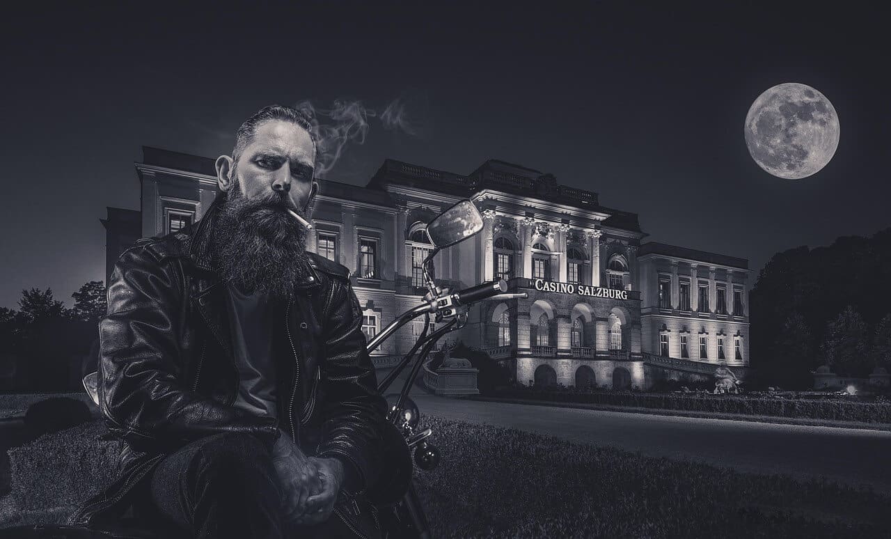 A man with a saxophone sits outside an illuminated historic building at night.