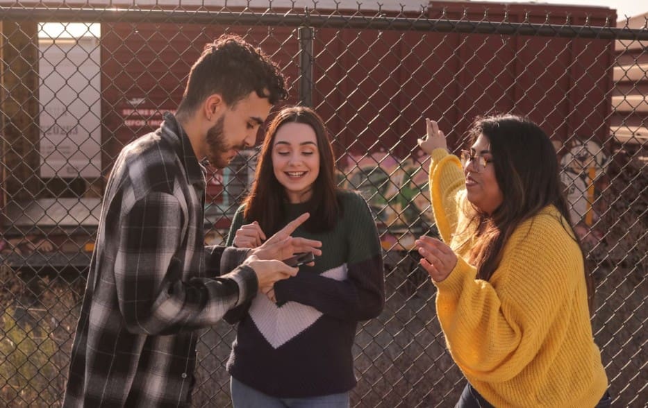 Three friends enjoying a moment while looking at their phones outdoors.