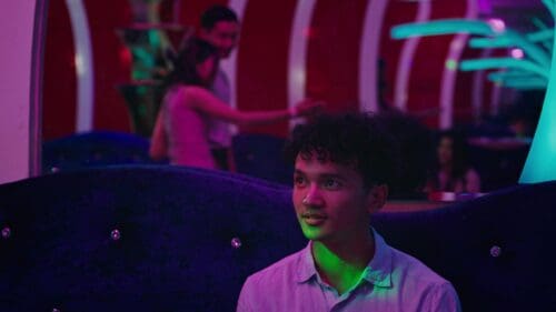 Young man sitting in a dimly lit room with colorful lighting.
