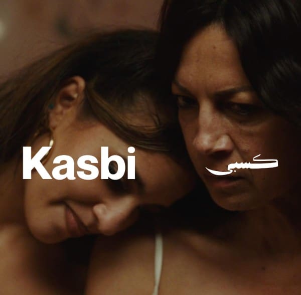 Two women close together, one resting her head on the other's shoulder with text "Kasbi".