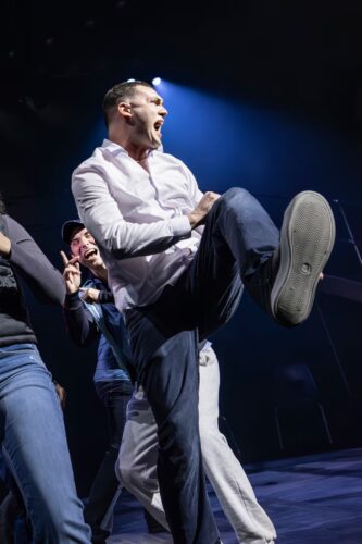 Man passionately singing on stage with lively energy.