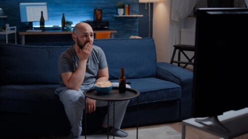 focused-man-looking-at drama-movie-crying-and sitting-on sofa-eating-popcorn
