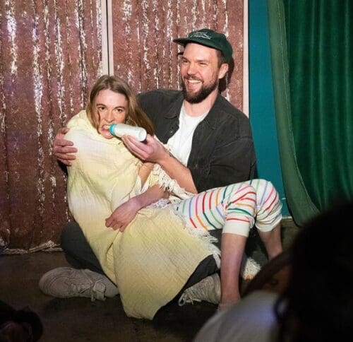 Rachel Troy performing BABY, an immersive solo clown show exploring attachment and emotional regression (an audience member holds a milk bottle).
