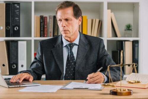 mature-man-using-laptop-while-checking-document-paper-courtroom