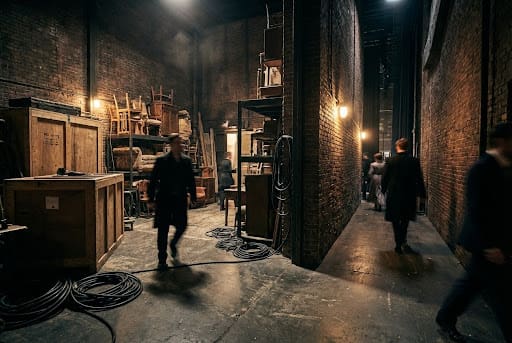 Backstage area with props, cables, and people moving around.