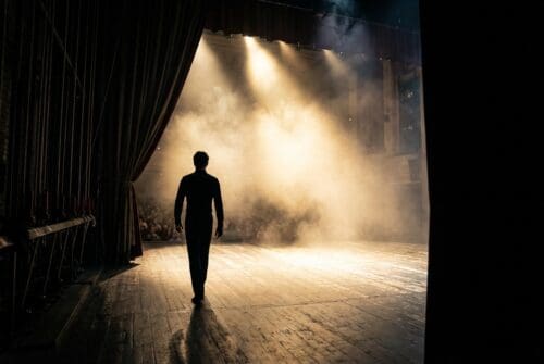 A lone performer walks onto a foggy stage.